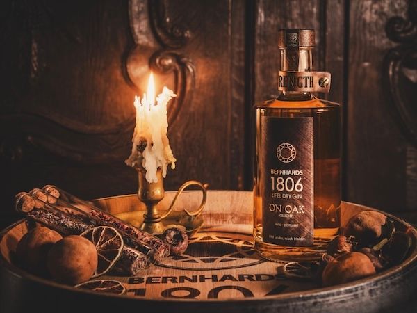 Bernhards 1806 Eifel Dry Gin On Oak neben Kerze und Gewürzen